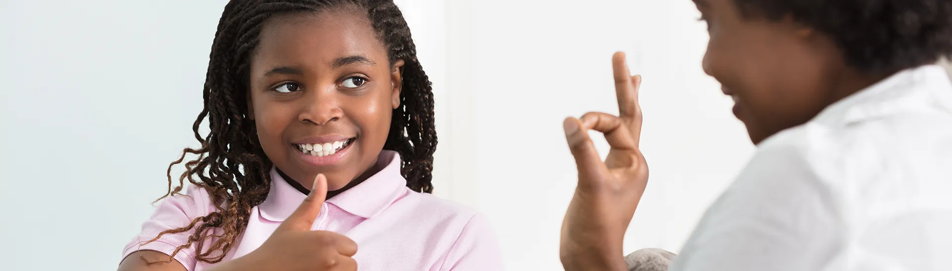 A black girl giving a thumbs up to a black woman, both people are smiling.