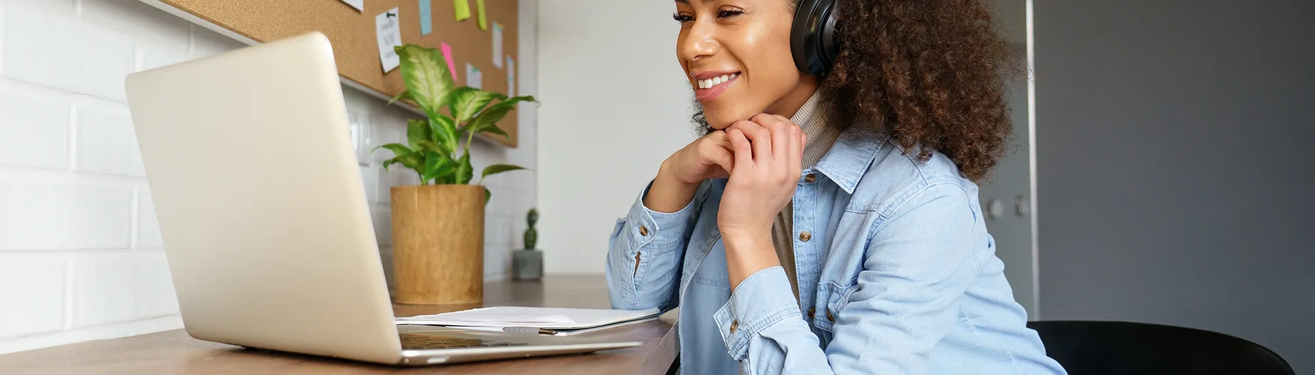 Black woman working with a headset on in front of her laptop computer.