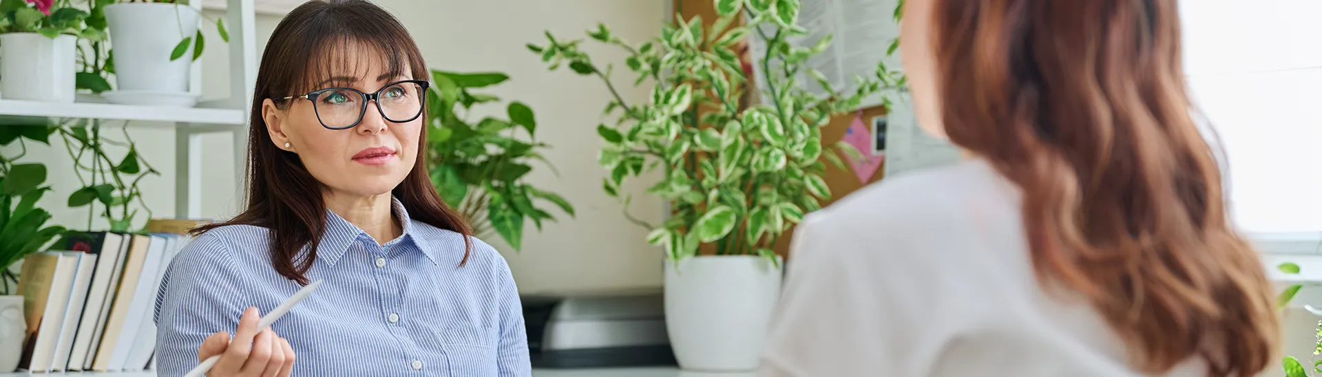 A female patient sitting, talking with a therapist who is holding a pen to take notes.