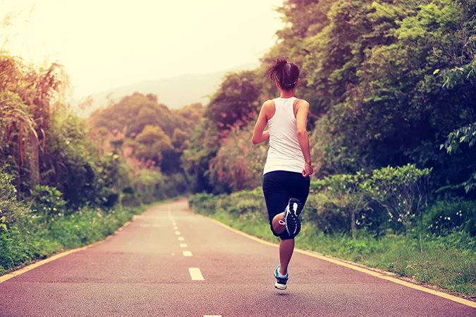 Woman running down a trail or path with grass and trees on either side.