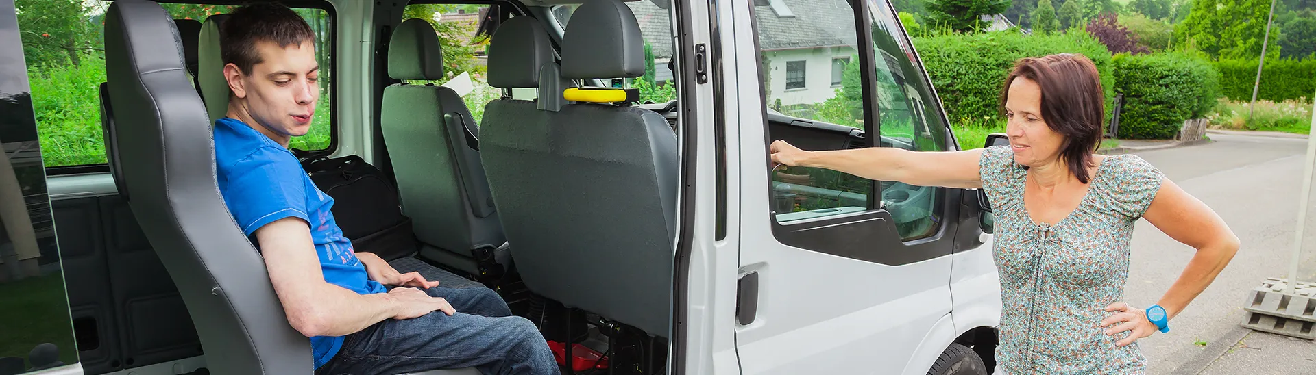 Handicap boy in van is getting ready to get out and into his wheelchair while woman rest her arm on the van door.